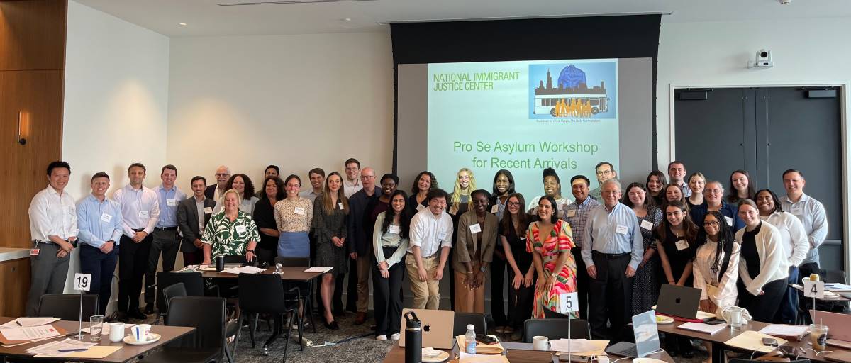 A group of about 40 volunteer attorneys and interpreters smile and pose in a conference room where they held a legal workshop to help people apply for asylum