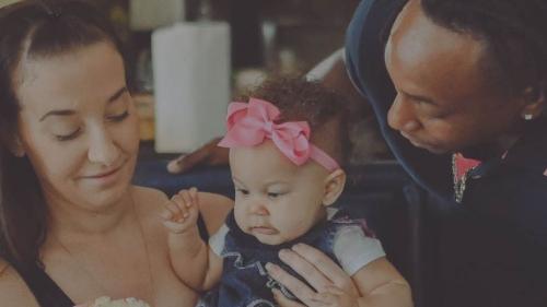 A mother holds a baby on her lap while the father looks down adoringly.