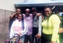 A photo of Jean with his arms around two of his children, with his two other children in front of and next to the group. All are posing with smiles for the camera.